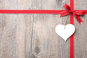 A wooden table with a red ribbon and heart on it.